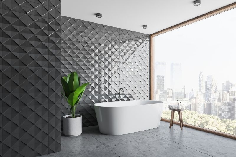 black tiled bathroom wall having indoor plants and bath tub near the crystal window