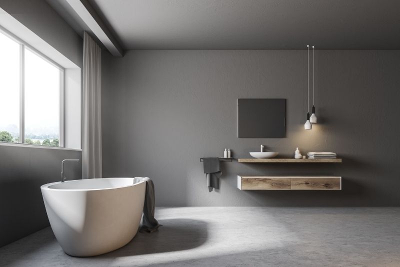 grey coloured bathroom wall having bath tub near the window and sink and mirror in the center